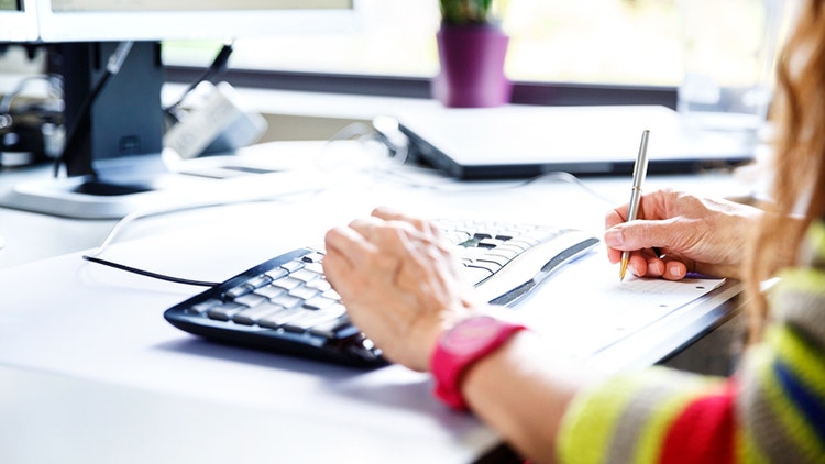 Persoon achter toetsenbord aan het schrijven met pen
