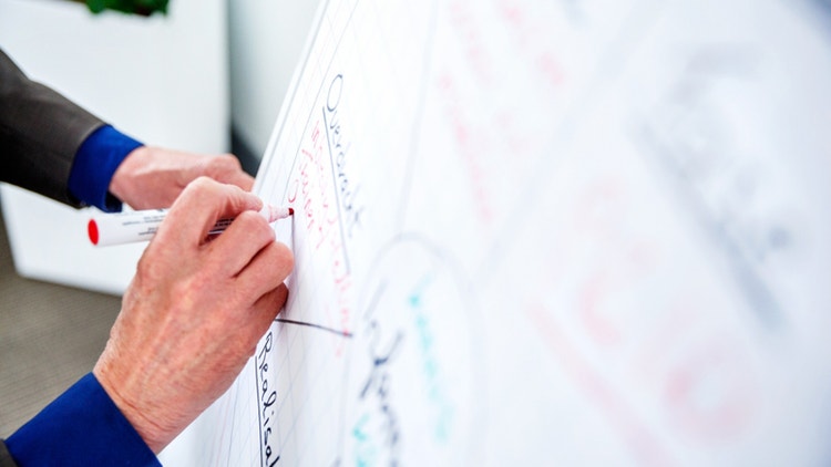 Persoon schrijft met markeerstift op een whiteboard